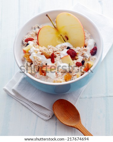 Delicious homemade muesli with fruit including fresh halved and diced apple and dried apricots and raisins and nuts served in a bowl on a white wooden rustic table