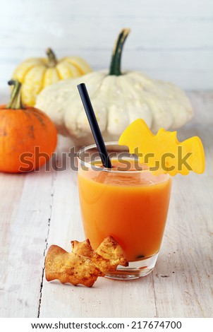 Glass of Halloween juice or vegetable smoothie served with a straw and scary bat shaped cookies and garnsih on rustic white wooden boards with pumpkins