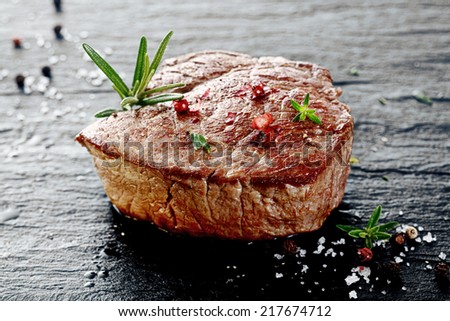 Succulent thick grilled beef steak trimmed for fat for a healthy diet on a griddle with a sprig of fresh rosemary and seasoned with salt and peppercorns