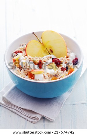 Bowl of healthy breakfast cereal with a halved fresh apple and topped with diced apple, dried fruit and nuts served with milk in a blue ceramic bowl, high angle view