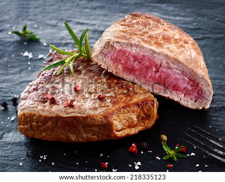 Two portions of lean trimmed grilled beef steak cut through to show the succulent tender red meat and seasoned with rosemary, salt and pepper in a steakhouse or restaurant