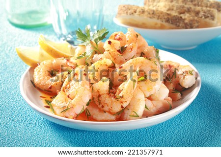 Tasty grilled shelled pink shrimps or prawns seasoned with olive oil and herbs served as a seafood starter to a meal on a textured blue table