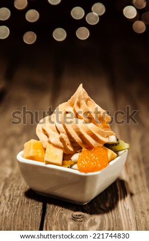 Tangy orange, mandarine or tangerine citrus frozen yogurt with fresh fruit salad in a owl on a rustic wooden table with copyspace and a bokeh of sparkling party lights