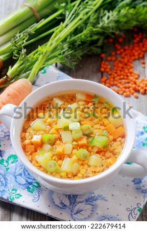 Delicious nutritious country cuisine with a bowl of carrot, leek and lentil vegetable soup, high angle view with bunches of fresh leeks and carrots and dried lentils