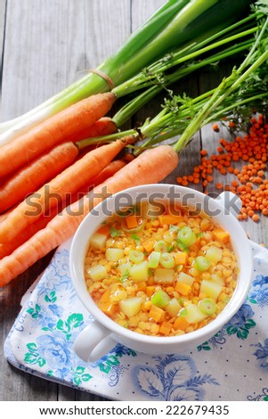 Nutritious lentil, carrot and leek soup served in a bowl surrounded by fresh bunches of carrots, leeks and dried orange lentils