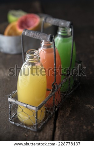 Three full bottles of natural juice, yellow, orange and green, made from squeezed citrus fruits as lemon, grapefruit and green pomelo, in a metallic rustic basket, on a wooden table
