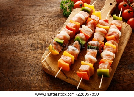 Tasty uncooked meat kebabs in a country kitchen with cubed meat, diced colorful bell peppers, onion and tomato on a wooden chopping board ready to grill on a wooden scored grungy counter top