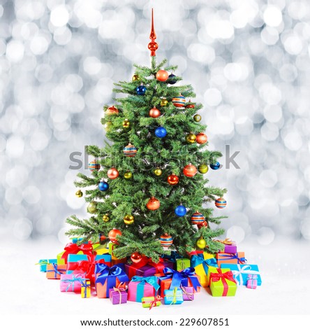 Colorful family Christmas tree surrounded by multiple gifts in the colors of the rainbow standing against a bokeh of falling fresh white snow with copyspace
