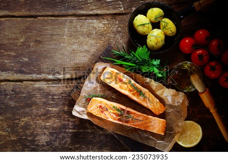 Overhead view of delicious grilled savory salmon cutlets with ingredients including a bouquet garni of fresh herbs, olive oil, tomatoes, baby potatoes and lemon on a rustic wood table with copyspace