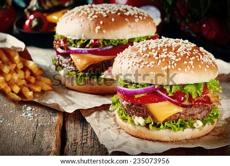 Two cheeseburgers on sesame buns with succulent beef patties and fresh salad ingredients served with French Fries on crumpled brown paper on a rustic wood table