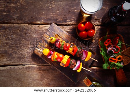 Delicious bar lunch of fresh vegan or vegetarian kebabs with assorted roasted colorful vegetables on skewers served on a rustic wood table with a beer and salad, with copyspace