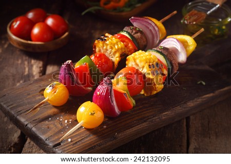 Colorful vegan or vegetarian vegetable skewers with fresh roasted or grilled sweet peppers, onion, mushroom, corn, eggplant and cherry tomatoes, close up view on a wooden board