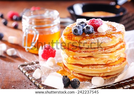 Stack of fresh golden pancakes or flapjacks topped with fresh autumn berries and drizzled with honey or syrup and white sugar