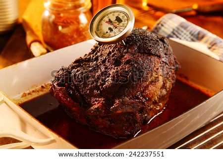 Whole roast shoulder of pulled pork in a roasting pan with a rich spicy marinade and thermometer to check the cooking time and tenderness