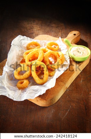 Cooked Mouth Watering Squid Rings with Sour Cream Sauce on White Paper Above Wooden Serving Board.