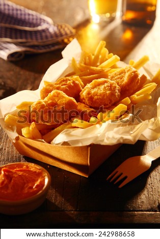 Takeaway carton of fried fish in crispy batter with French fries and a dipping sauce served with beer in a pub or cafeteria
