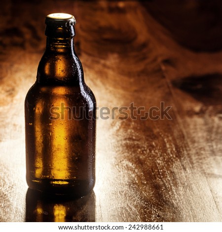 Unlabeled unopened brown bottle of cold beer standing on a wooden bar counter with copyspace for your advertising