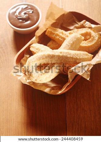 Close up Delicious Churros Snacks on Tray, with Paper, with Chocolate Dipping Sauce on Side. Placed on Wooden Table.