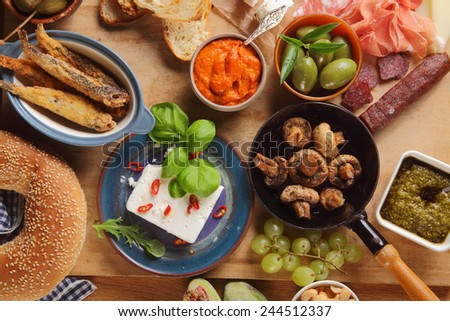 Close up Assorted Tapas Foods on Wooden Table, Emphasizing Cheese, Mushrooms, Meats, Bread, Olives and Sauce.