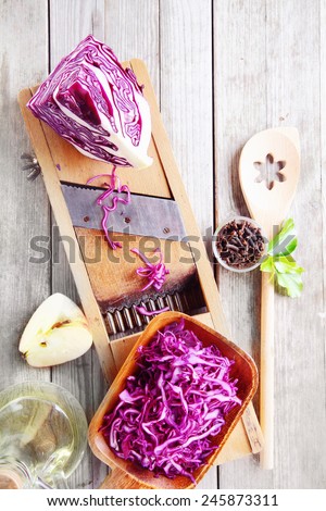 Close up Fresh Purple Cabbage and Apple Salad Ingredients on Wooden Table with Shredder and Wooden Ladle.