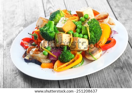 Healthy vegetarian cuisine with a tofu salad with colorful roast vegetables including sweet peppers, onion and mushrooms, peas and broccoli