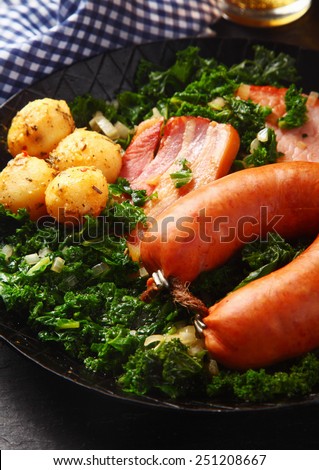 Close up Tasty German Recipe on a Frying Pan, Emphasizing Cooked Sausage, Pork Meat and Potatoes on Green Vegetables.