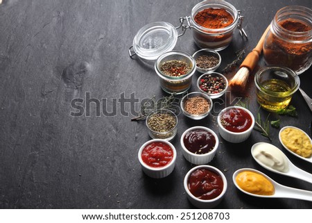 Close up Various Condiments on Containers and Spoons on Top of Black slate Table with Copy Space on the Left Side.