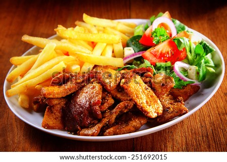 Close up Appetizing Healthy Meal Combination of Cooked Meat, French Fries and Fresh Veggies on Top of Brown Wooden Table.