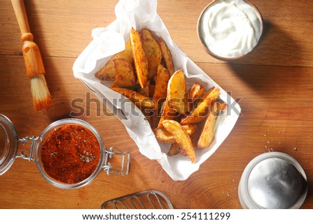 Close up Aerial Shot of Fried Potato Slices on White Paper with Cream Sauce and Powdered Spices on Top of Wooden Table.