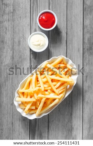 Close up Aerial Shot of Salted French Fries with Dipping Sauces on the Side at the Top of Wooden Table.
