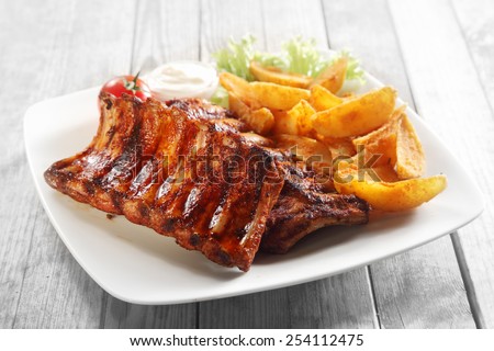 Close up Gourmet Main Dish with Grilled Pork Rib and Fried Potatoes on White Plate. Served on Wooden Table.