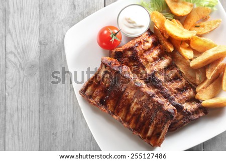 Close up Tasty Grilled Pork Rib and Fried Potatoes on White Plate with White Sauce on a Plate. Placed on Wooden Table With Copy Space.