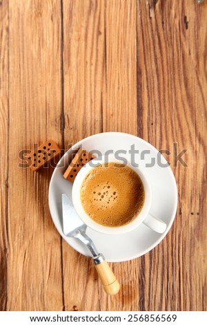 Aerial Shot of Cup of Brown Coffee on a Plate with Trowel and Small Wooden Bricks on Sides, Placed on Top of a Wooden Table, Emphasizing Copy Space.