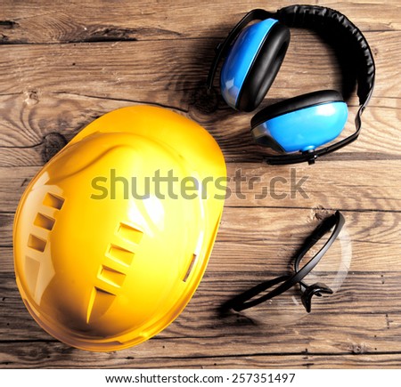 Close up Safety Engineer Gears- Yellow Helmet, Transparent Goggles and Black and Blue Ear Defenders on Top of the Wooden Table.