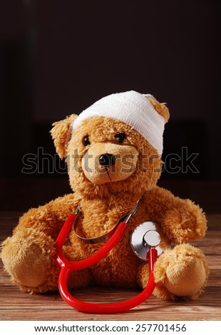 Close up Front View of Bandaged Plush Teddy Bear with Stethoscope Device on Top of the Wooden Table.