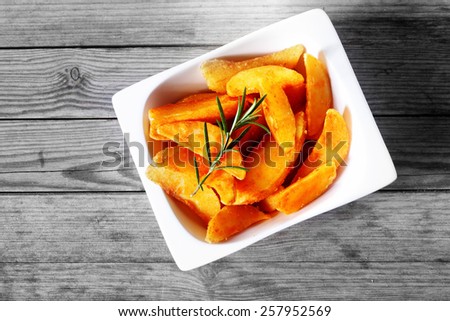 Close up Aerial Shot of Crispy Fried Potatoes in a White Bowl, with Rosemary on Top, Served on Wooden Table.