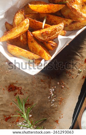 Close up Hot Spicy Potato Wedges on White Plate on Top of Oiled Paper with Powder Residue and Herbs