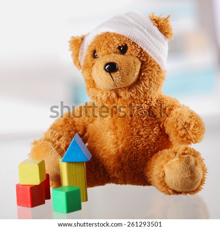 Close up Classic Brown Teddy Bear with Bandage on the Head Sitting on the Table with Assorted Block Shapes.