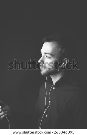 Man listening to music on an  player standing holding the device in his hand listening to the tunes over earplugs, greyscale image with copyspace
