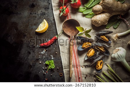 Freshly cooked mussels with savory ingredients for preparing a gourmet seafood appetizer including garlic, chili pepper, root ginger, tomatoes, coriander, bay leaf and spices with a rustic wood spoon