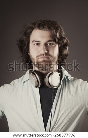 Close up Portrait of a Serious Young Man with Headphone Around his Neck, Looking at the Camera on a Brown Gradient Background.