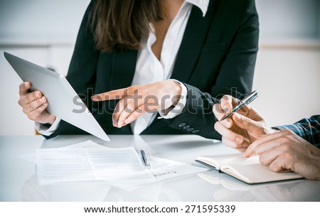 Businesswoman in a meeting sitting at a table with a make colleague pointing to her tablet, close up view of their hands
