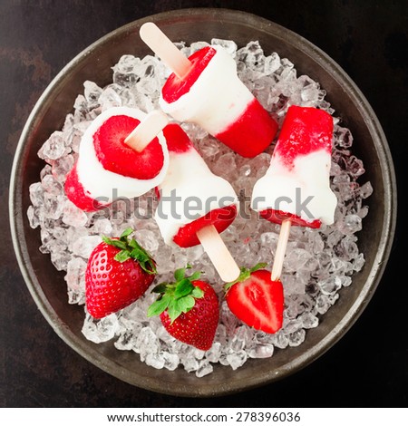 Healthy frozen strawberry dessert with the pulp of fresh ripe red strawberries combined into a refreshing homemade sucker with frozen yogurt or ice cream served in a bowl of crushed ice