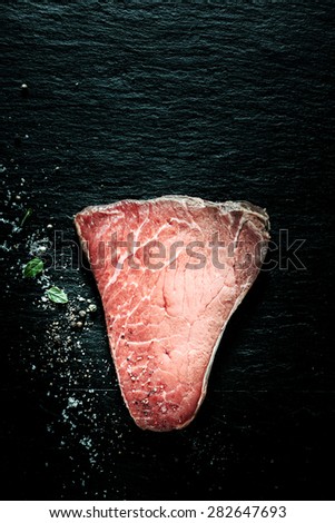 High Angle View of Marbled Round Top Beef Steak Seasoned with Fresh Herbs and Spices on Dark Textured Surface with Copy Space