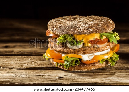 Single Healthy Looking Burger Piled with Fresh Vegetables and Sauces on Whole Grain Bun, on Rustic Wooden Surface with Copy Space