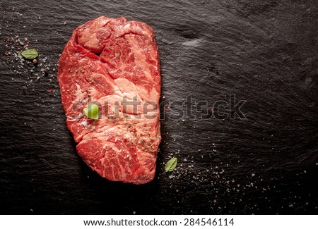 High Angle View of Raw Chuck Eye Beef Steak Seasoned with Herbs and Spices on Dark Grey Textured Surface with Copy Space