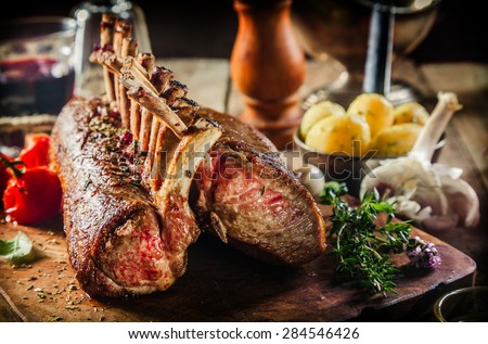 Roasted Rectangle Rack of Lamb Chops on Wooden Cutting Board Surrounded by Herbs and Fresh Ingredients