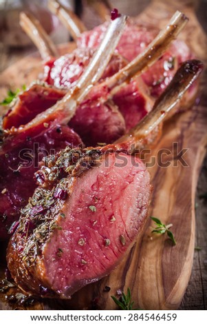 Close Up of Rare Rectangle Lamb Chops Sliced and Seasoned with Fresh Herbs on Wooden Cutting Board