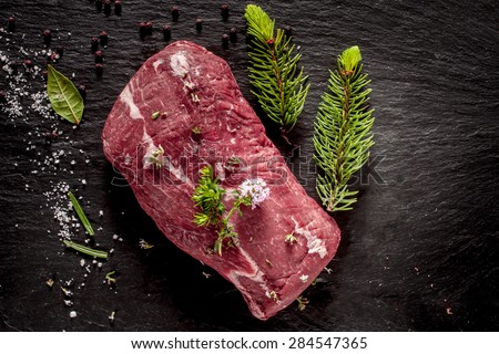 High Angle View of Raw Beef Roast Seasoned with Fresh Herbs and Spices on Dark Grey Textured Surface