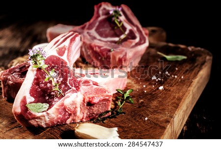 Close Up of Raw Lamb Filets Seasoned with Garlic, Salt and Fresh Herbs on Rustic Wooden Board